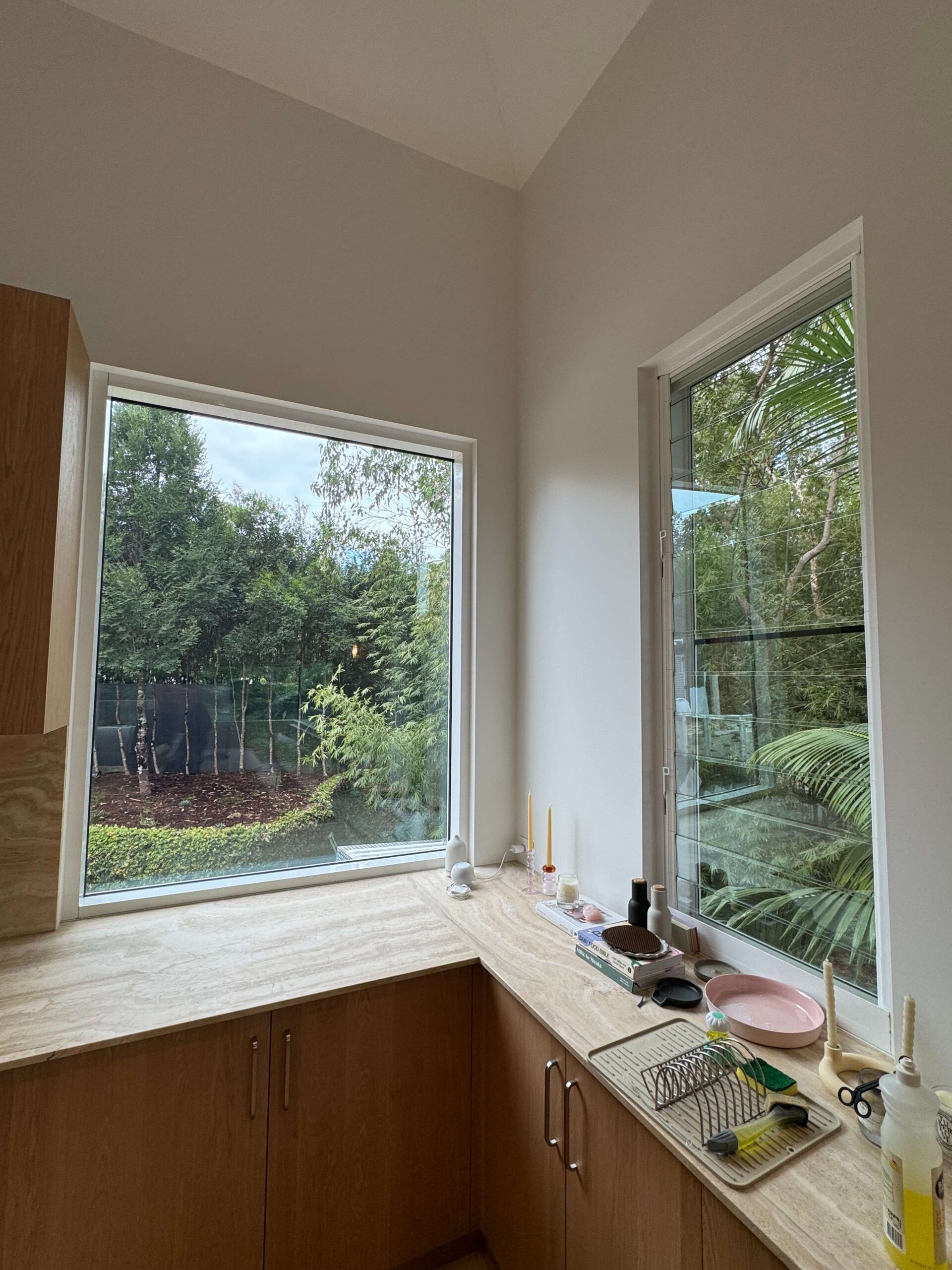 AGG Services kitchen interior with large window and clear louvre window offering a clear view of a lush green garden outside.